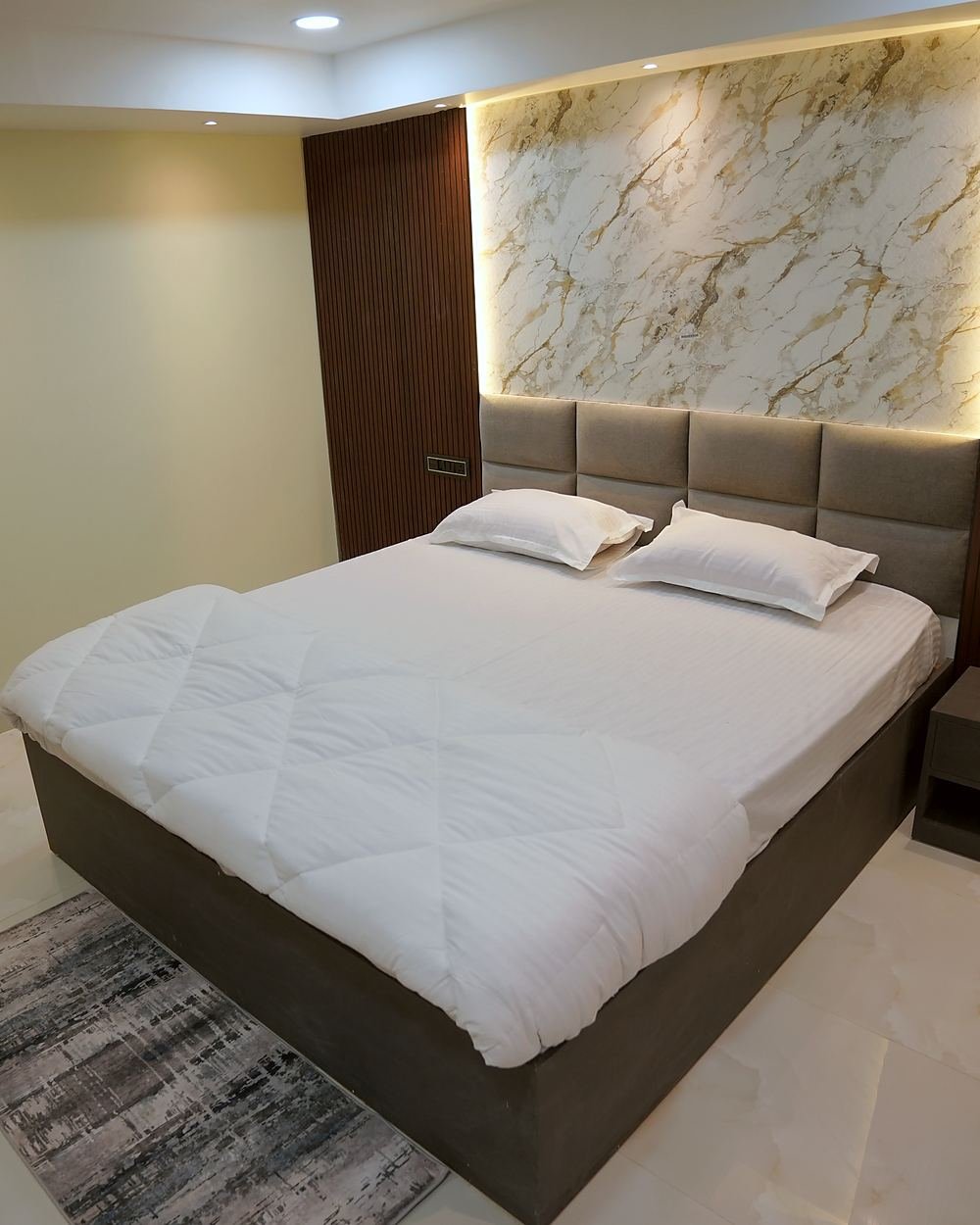 A Deluxe Room at Kamagiri Nivas, its bed set beneath a backlit marble panel framed in fluted wood