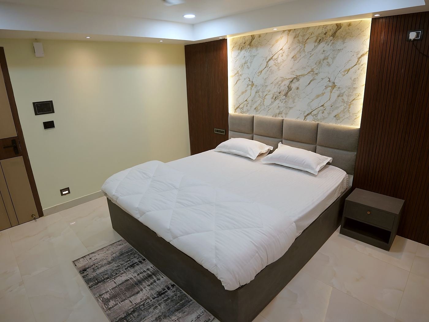 Deluxe Room — king bed beneath a backlit marble panel flanked by fluted wood